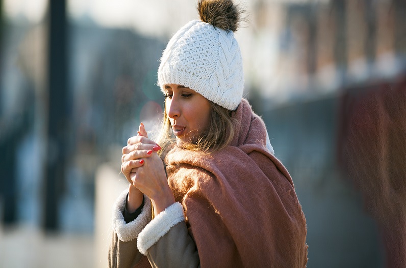 Woman breathing on her hands to keep them warm at cold winter